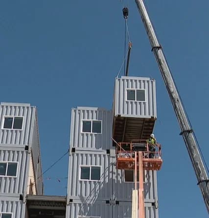 Crane lifting a shipping container module into a multi-story modular building