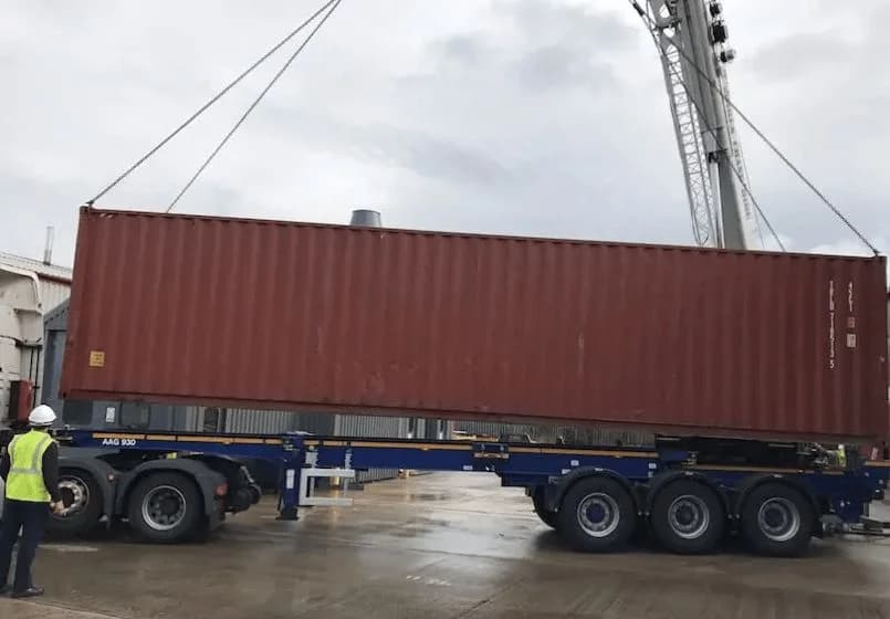 Crane lifting a shipping container onto a flatbed trailer