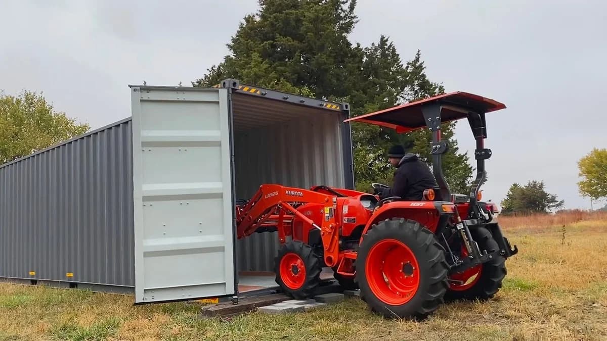 Red tractor parked in front of a shipping container on a farm